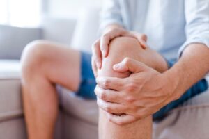 Man sitting on sofa, holding his painful knee